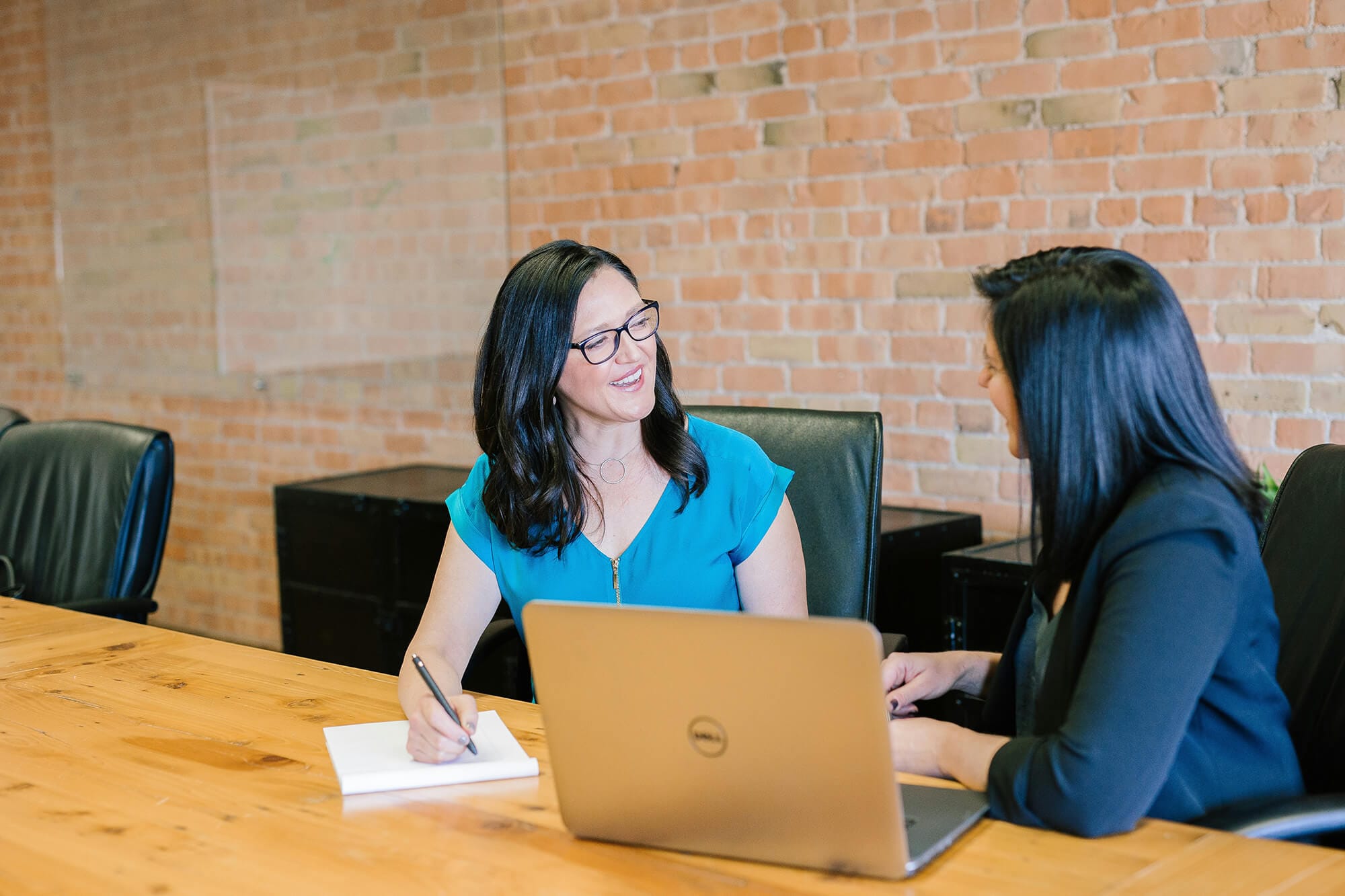 Two women talking in front of a laptop and taking notes